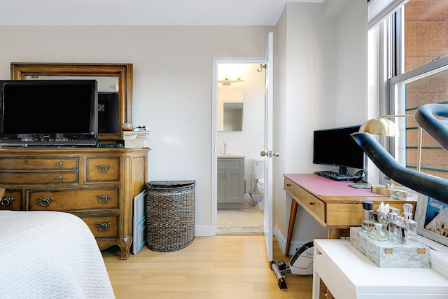 bedroom with connected bathroom, baseboards, and light wood-style flooring