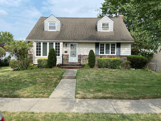 cape cod-style house with stone siding, a front lawn, and a shingled roof