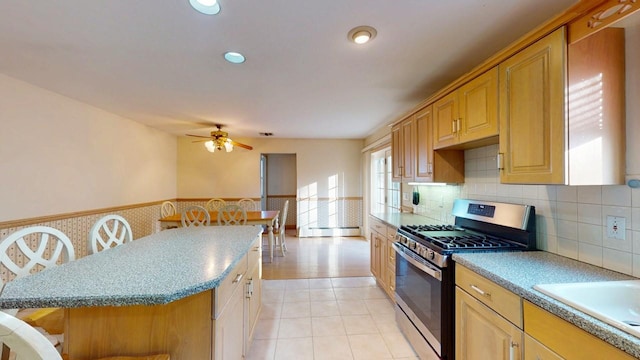 kitchen featuring a breakfast bar area, a ceiling fan, a wainscoted wall, stainless steel range with gas stovetop, and a center island