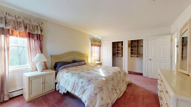 bedroom featuring a baseboard heating unit, dark colored carpet, and two closets