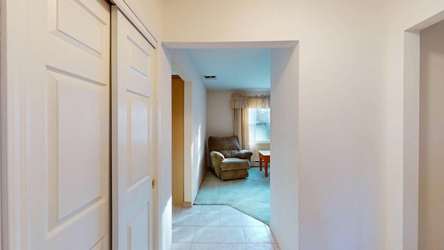 hallway with light tile patterned flooring, light colored carpet, visible vents, and baseboards