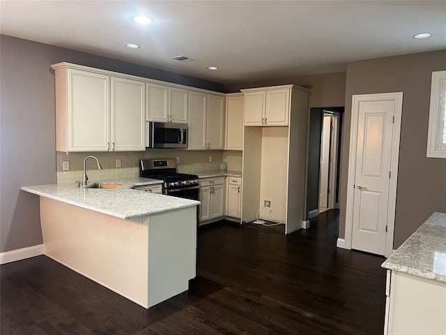 kitchen featuring visible vents, appliances with stainless steel finishes, a peninsula, dark wood-style floors, and a sink