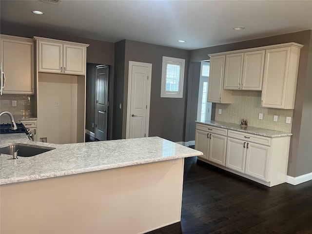 kitchen featuring a sink, light stone counters, tasteful backsplash, a peninsula, and dark wood-style flooring