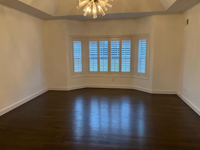 empty room featuring dark wood-style floors, baseboards, a tray ceiling, and an inviting chandelier