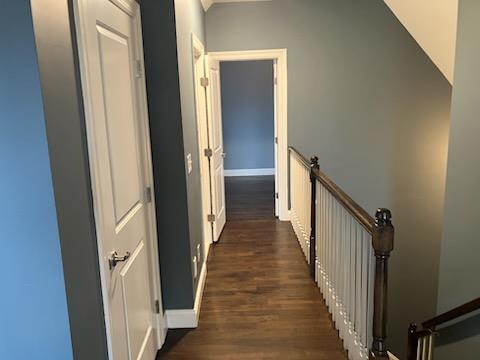 corridor featuring baseboards, an upstairs landing, and dark wood-style floors