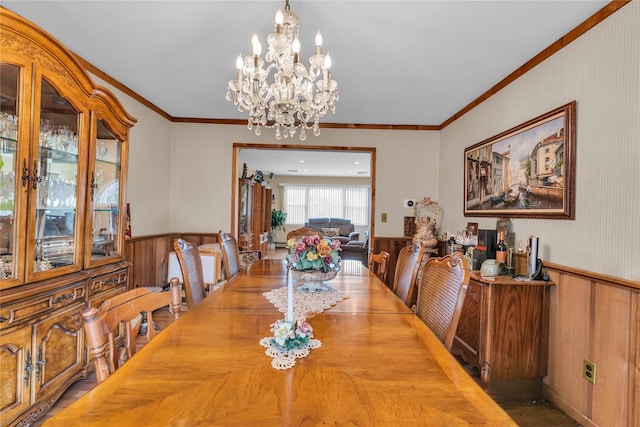 dining room featuring a notable chandelier, wooden walls, wainscoting, and ornamental molding