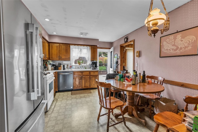 kitchen with a sink, light countertops, appliances with stainless steel finishes, brown cabinetry, and light floors
