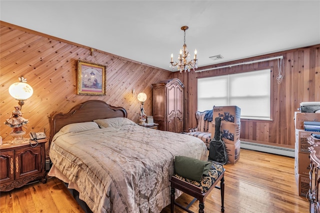 bedroom with an inviting chandelier, wooden walls, visible vents, a baseboard heating unit, and light wood finished floors