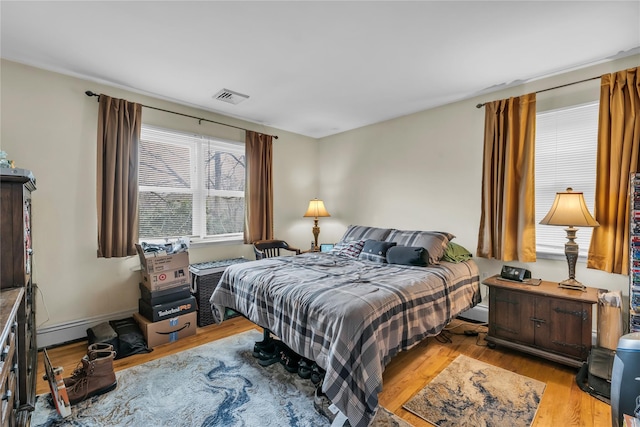 bedroom with light wood-style floors, visible vents, and a baseboard radiator