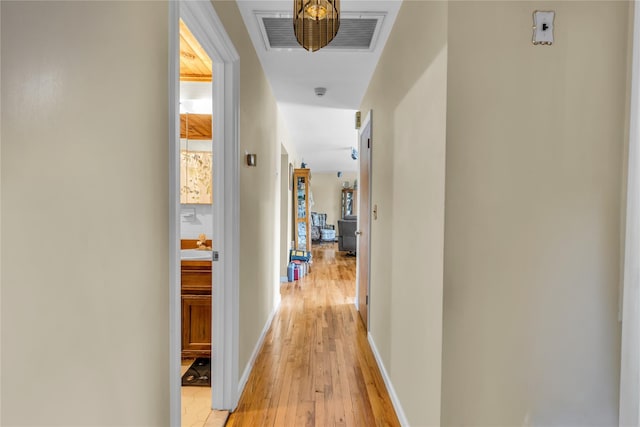 hallway featuring visible vents, light wood-style flooring, and baseboards