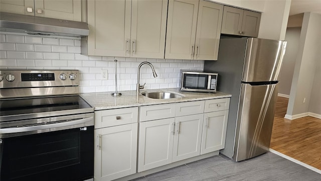 kitchen featuring under cabinet range hood, a sink, tasteful backsplash, light wood-style floors, and appliances with stainless steel finishes