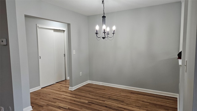 unfurnished dining area featuring a chandelier, dark wood-style floors, and baseboards