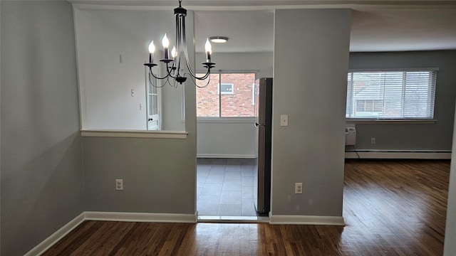 unfurnished dining area featuring dark wood-style floors, baseboard heating, baseboards, and an inviting chandelier