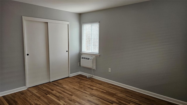 unfurnished bedroom featuring an AC wall unit, wood finished floors, baseboards, and a closet