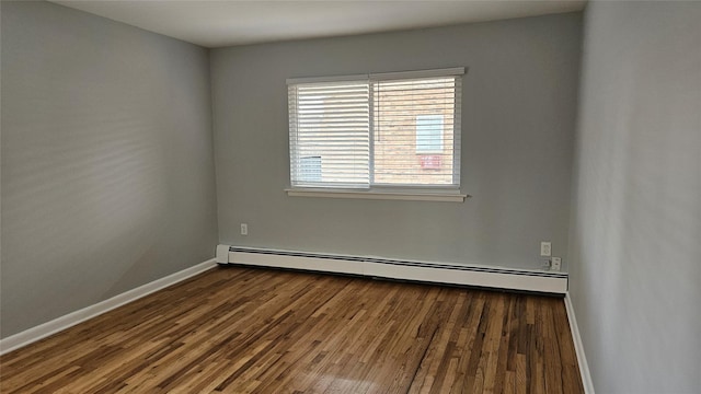 spare room featuring a baseboard heating unit, baseboards, and wood finished floors