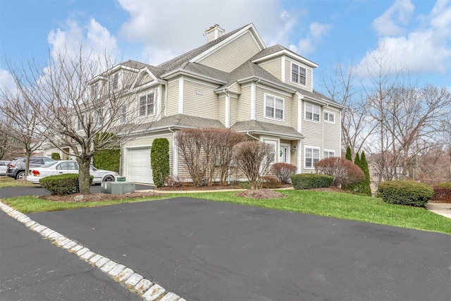 shingle-style home with a garage, driveway, and a chimney