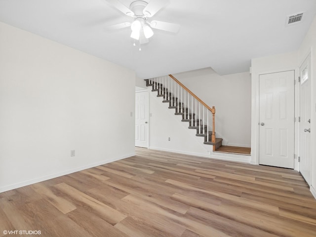 unfurnished living room featuring visible vents, light wood-style flooring, a ceiling fan, stairway, and baseboards