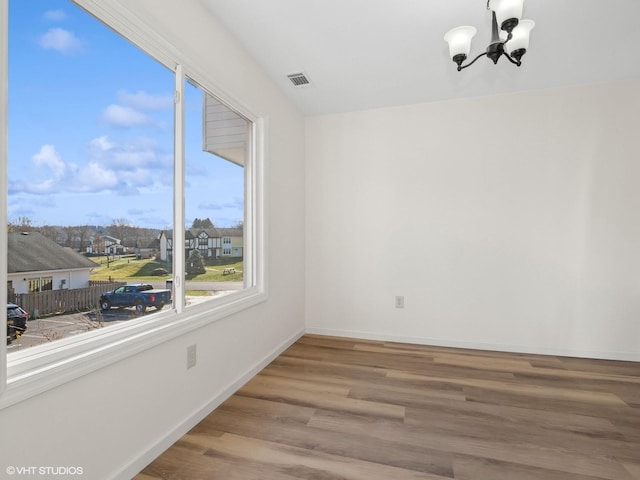 empty room with visible vents, wood finished floors, a residential view, an inviting chandelier, and baseboards