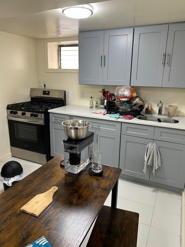 kitchen with a sink, light tile patterned flooring, stainless steel range with gas stovetop, and gray cabinets