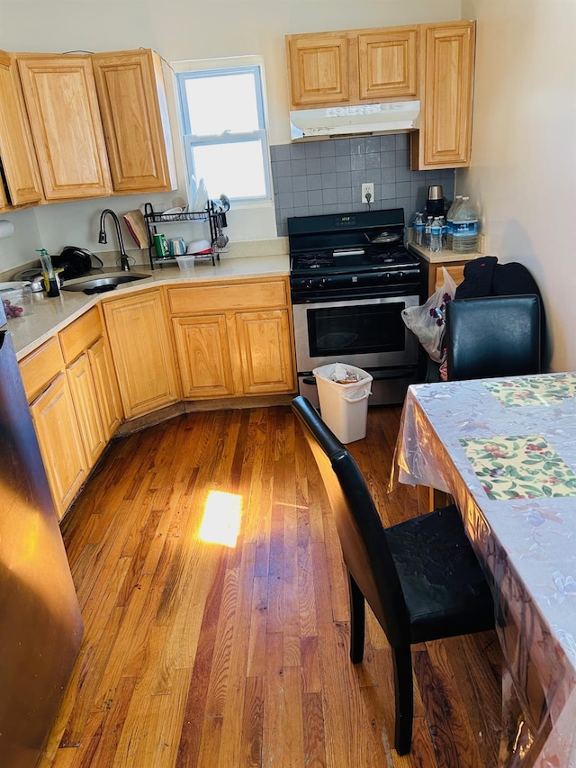 kitchen with light wood finished floors, a sink, light countertops, under cabinet range hood, and stainless steel gas stove