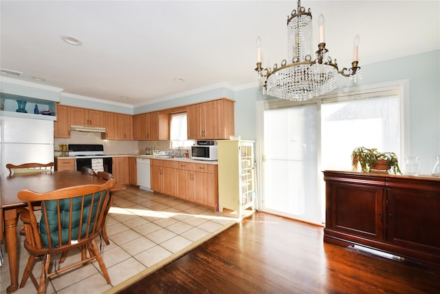 kitchen featuring under cabinet range hood, white appliances, an inviting chandelier, and crown molding