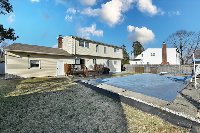 back of house featuring fence, a yard, a wooden deck, a fenced in pool, and a chimney