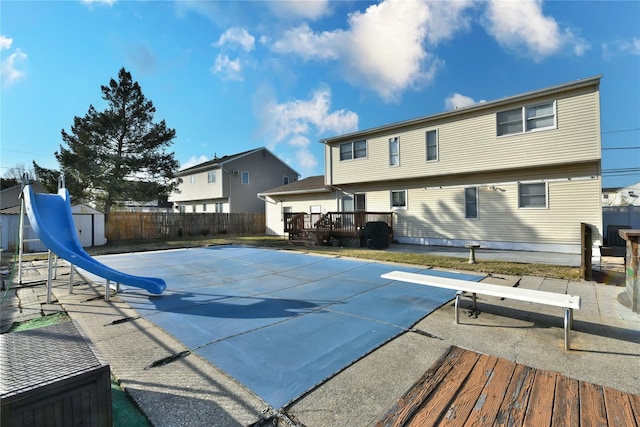 view of swimming pool with a water slide, a fenced backyard, an outdoor structure, a deck, and a storage shed