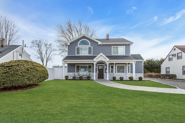 traditional-style house with stone siding, fence, a front yard, a shingled roof, and a chimney