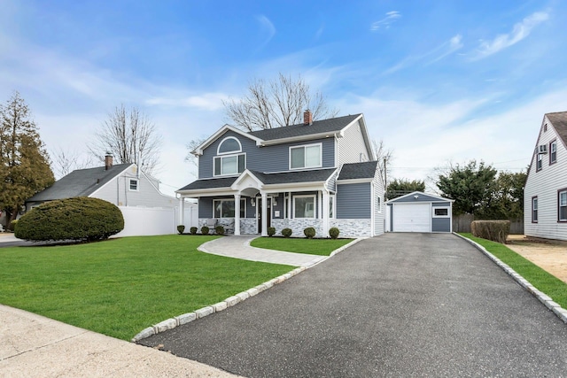 view of front facade with a front lawn, driveway, stone siding, fence, and an outdoor structure