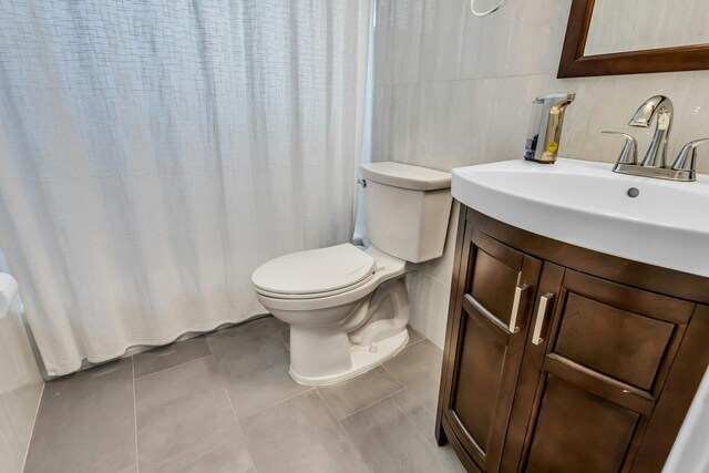 bathroom featuring tile patterned floors, toilet, curtained shower, tile walls, and vanity