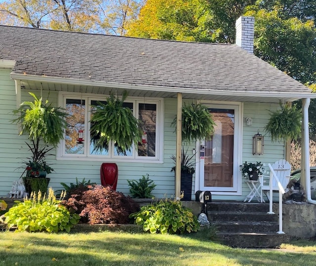 view of front of home with a front yard, a chimney, and a shingled roof