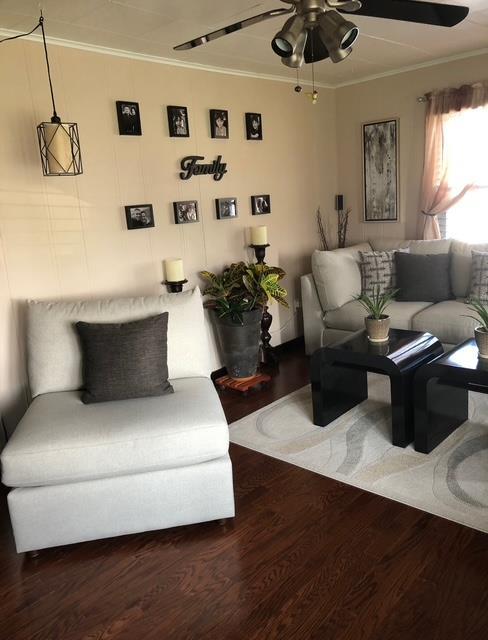 living area with crown molding, wood finished floors, and a ceiling fan