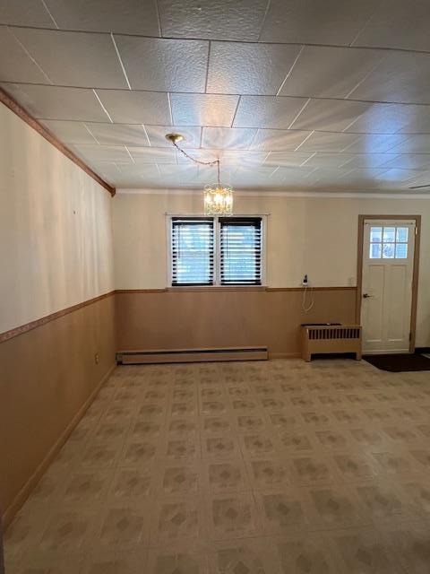 basement with a wainscoted wall, radiator heating unit, ornamental molding, a notable chandelier, and a baseboard radiator