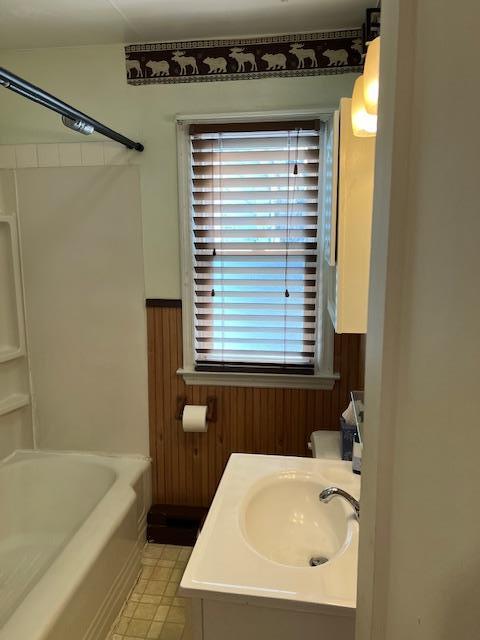 bathroom with vanity, wooden walls, bathtub / shower combination, and wainscoting