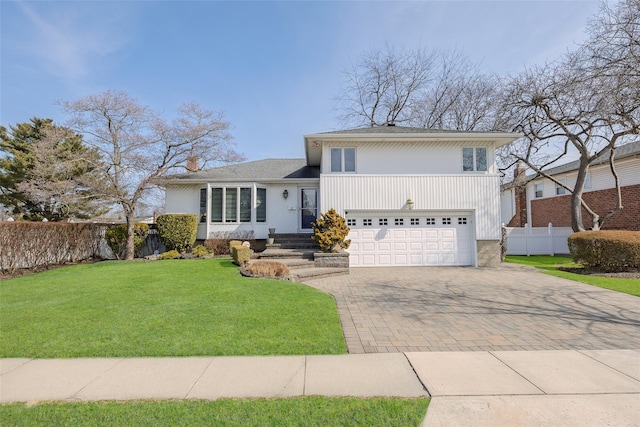 split level home with a front lawn, decorative driveway, fence, an attached garage, and a chimney