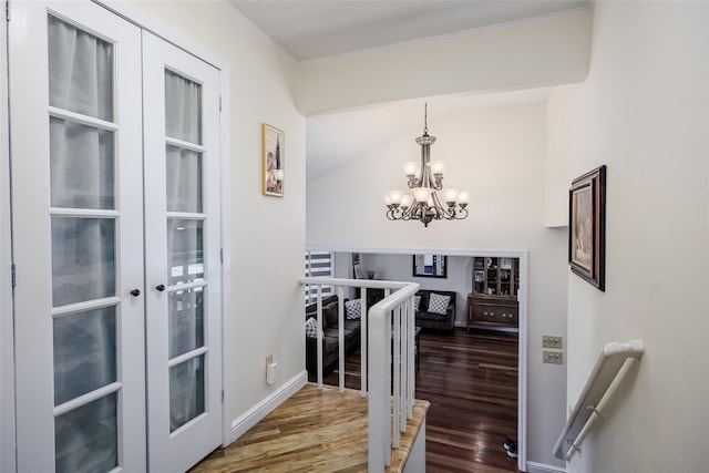 hallway featuring wood finished floors, baseboards, french doors, an upstairs landing, and a chandelier