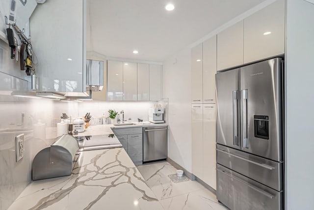 kitchen featuring modern cabinets, marble finish floor, a sink, appliances with stainless steel finishes, and light stone countertops