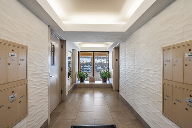 hall with mail area, a raised ceiling, and light tile patterned flooring