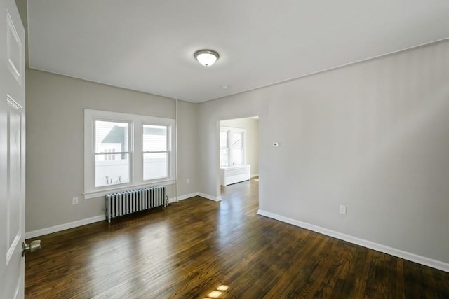 spare room featuring dark wood-style floors, radiator, and baseboards