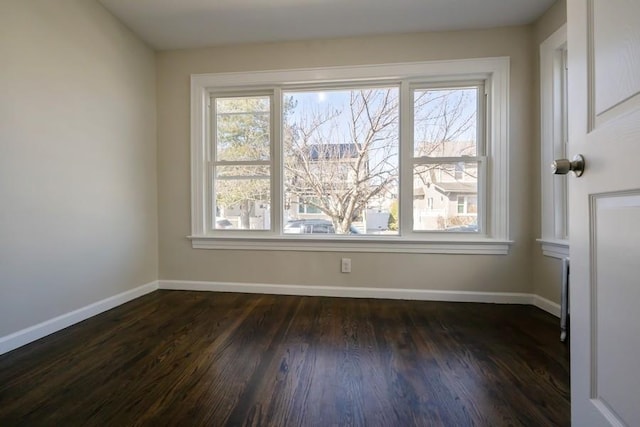 spare room with dark wood finished floors, a healthy amount of sunlight, and baseboards