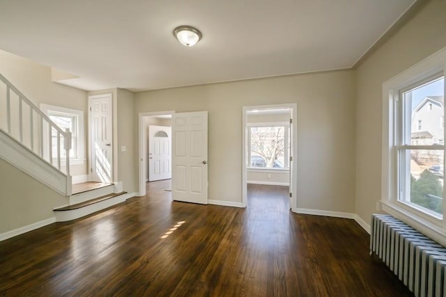 unfurnished living room with dark wood finished floors, stairway, radiator, and baseboards