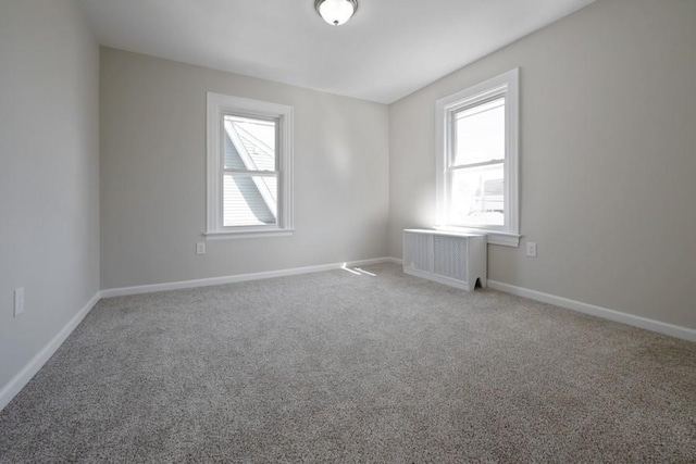 empty room with carpet flooring, a healthy amount of sunlight, radiator heating unit, and baseboards