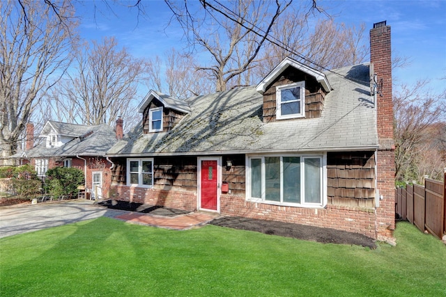 new england style home with a front yard, fence, brick siding, and a chimney