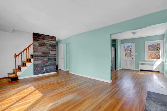 unfurnished living room featuring hardwood / wood-style floors, radiator, baseboards, and stairs