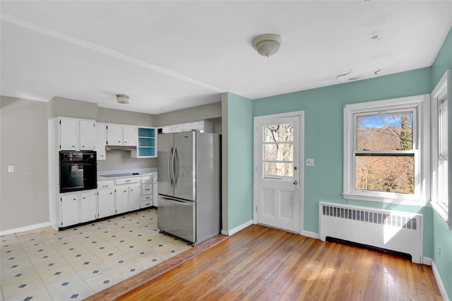 kitchen featuring light wood finished floors, radiator, black appliances, baseboards, and white cabinetry