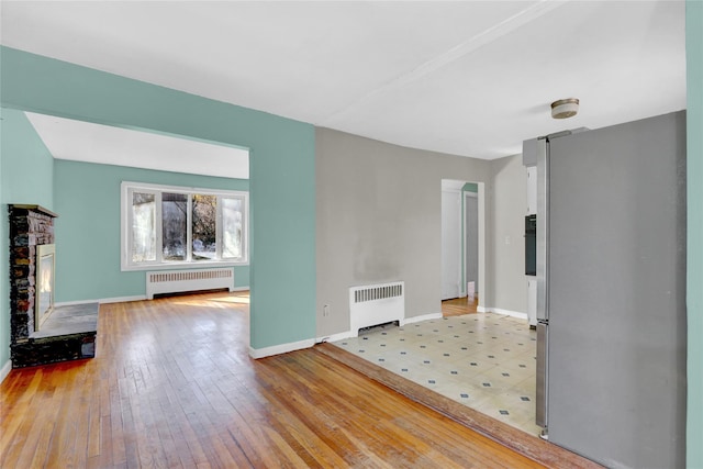 unfurnished living room with a glass covered fireplace, radiator heating unit, baseboards, and light wood finished floors