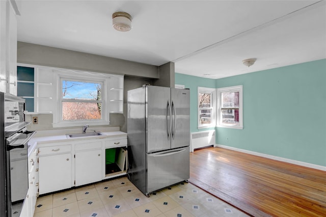 kitchen featuring a sink, freestanding refrigerator, radiator, white cabinets, and light countertops