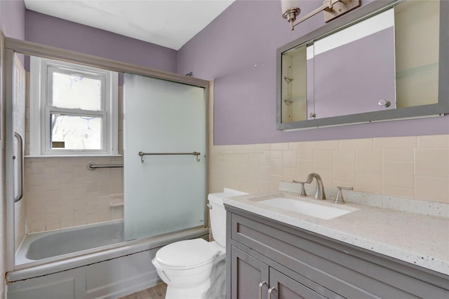 bathroom with a wainscoted wall, toilet, vanity, enclosed tub / shower combo, and tile walls