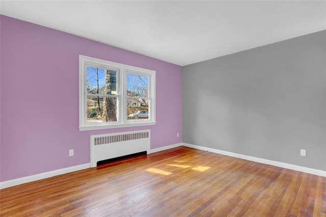 unfurnished room with baseboards, hardwood / wood-style floors, and radiator heating unit