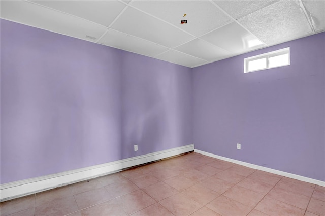 tiled empty room with a drop ceiling, baseboards, and baseboard heating